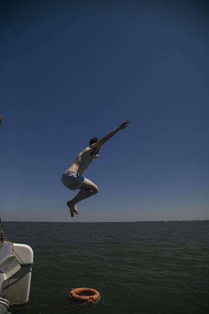 Lisbon: Catamaran Boat Party with Music, Open Bar & Dives - The 25 de Abril Bridge overhead